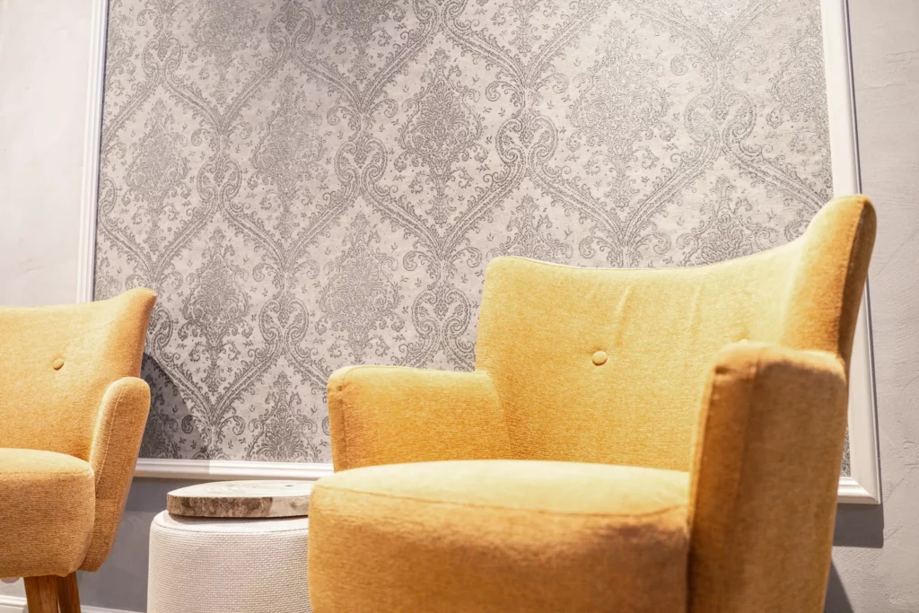 Ausschnitt aus dem Showroom. Zwei gelbe Sessel vor einer Wand mit barockem Muster in Grautönen.